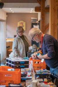 Repair Cafe in Laren, 2 reparateurs staan om een tafel op zoek naar spullen.